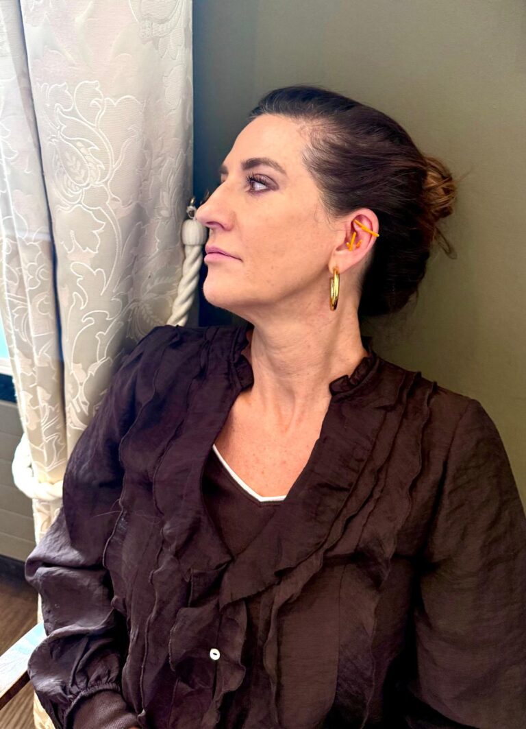 A participant seated in profile with small gold ear needles in her ear
