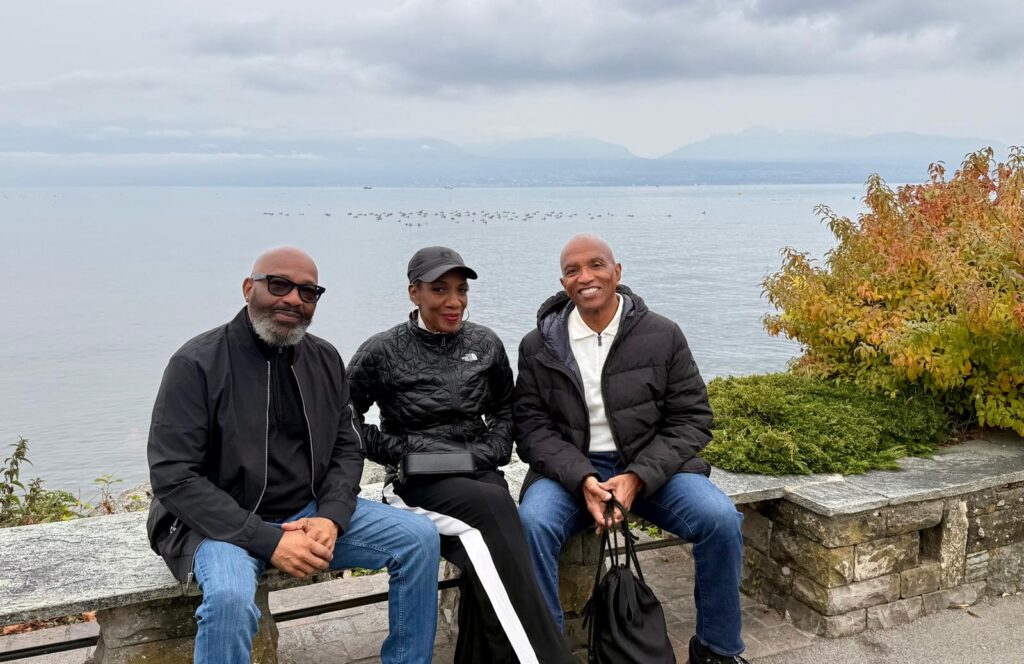 Three men sitting together on a stone wall beside the lake