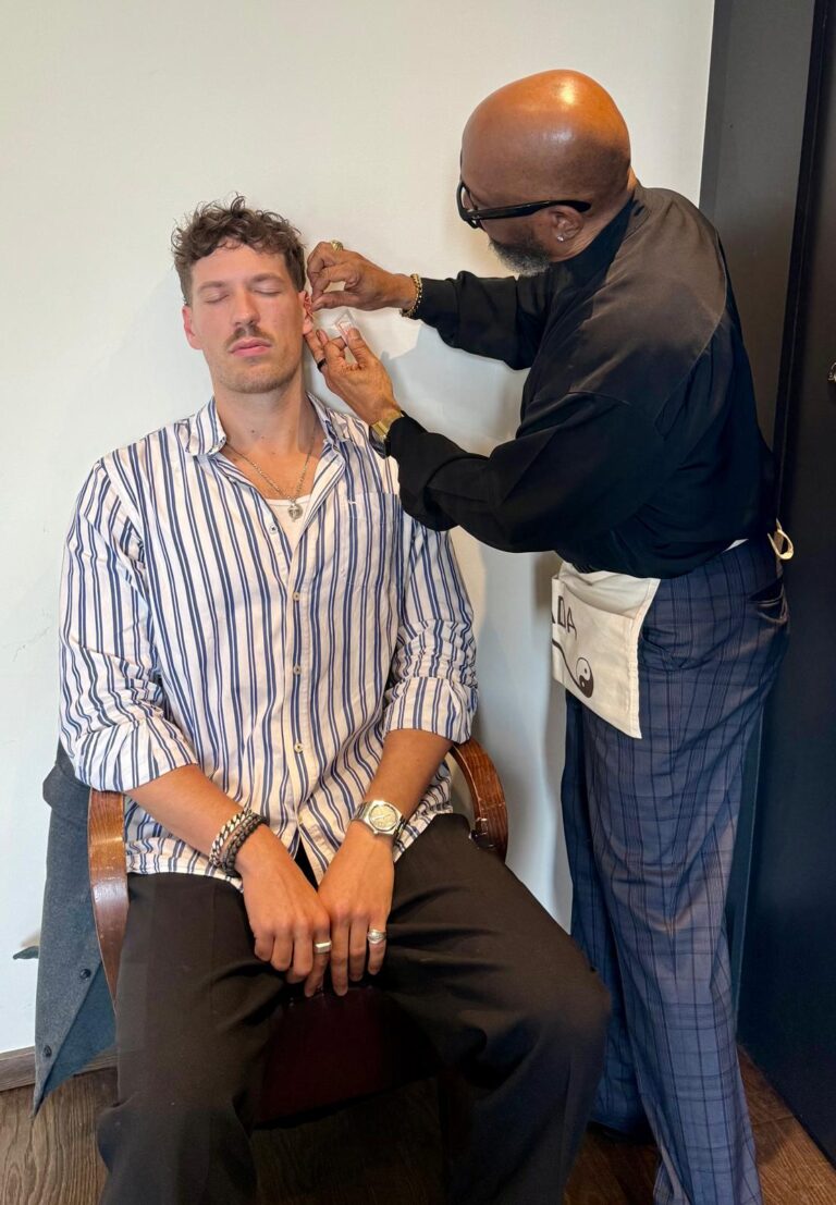 A trainer placing needles in the ear of a seated participant