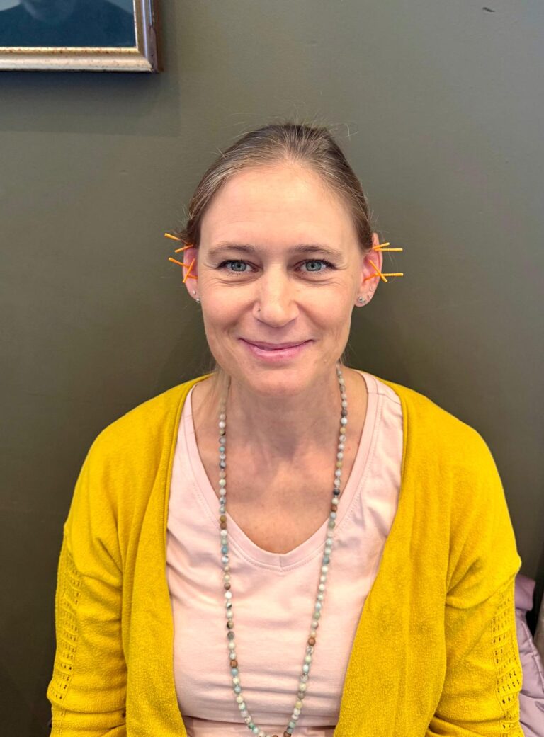 A smiling participant in a yellow cardigan with ear needles in place